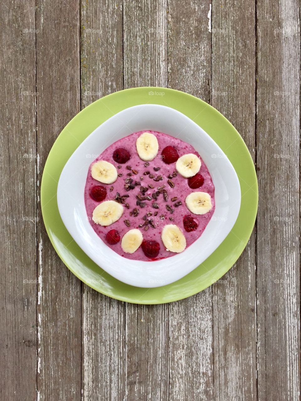 Fruits! - smoothie bowl made with raspberry, banana and coconut milk, topped with cacao nibs and fresh fruit, in white bowl on green plate, weathered wood surface