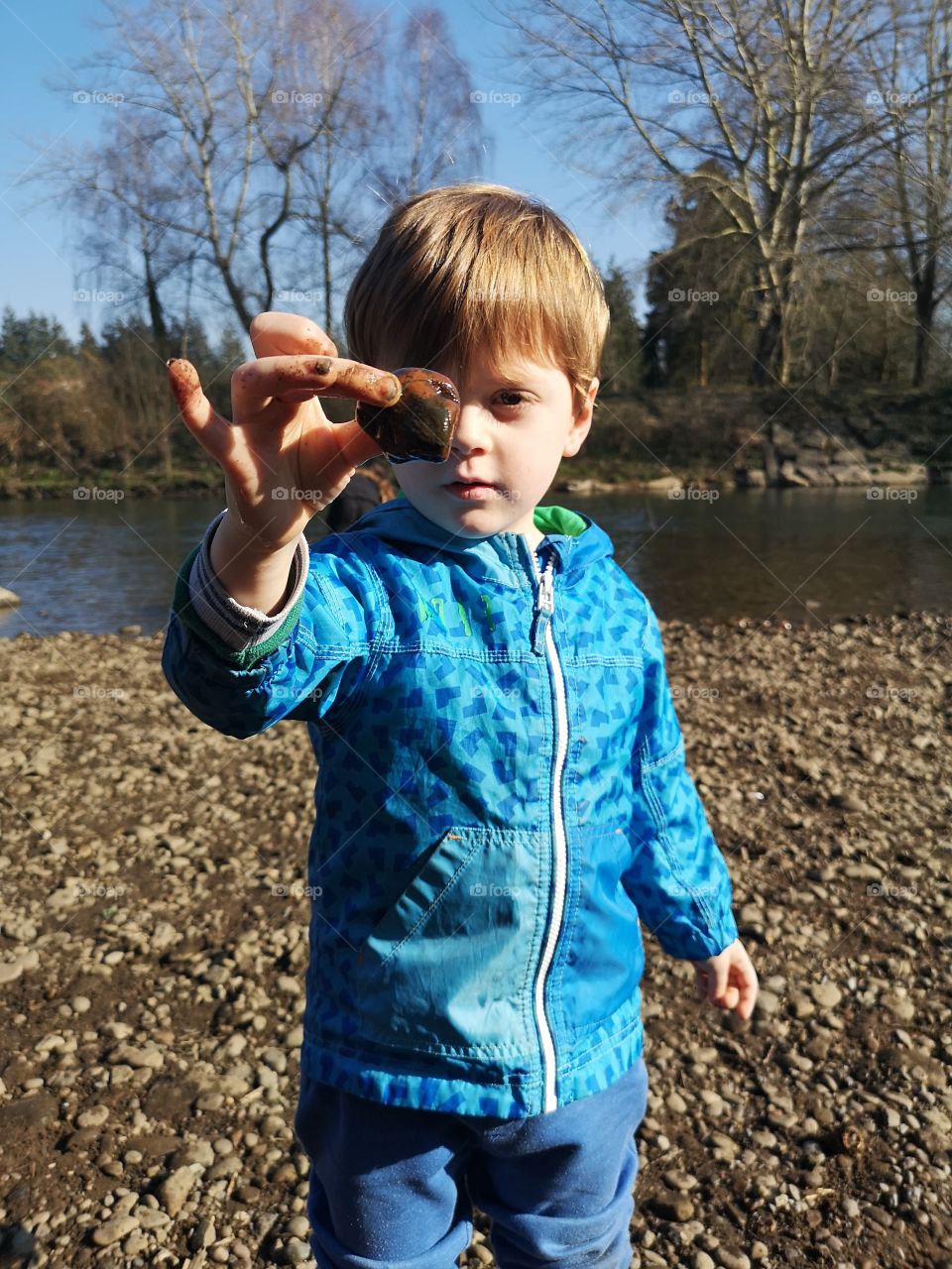 young boy proudly holds up a rock he found by the river