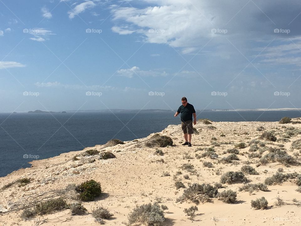 Man walking on cliff overlooking ocean in south Australia on blue sky clear day