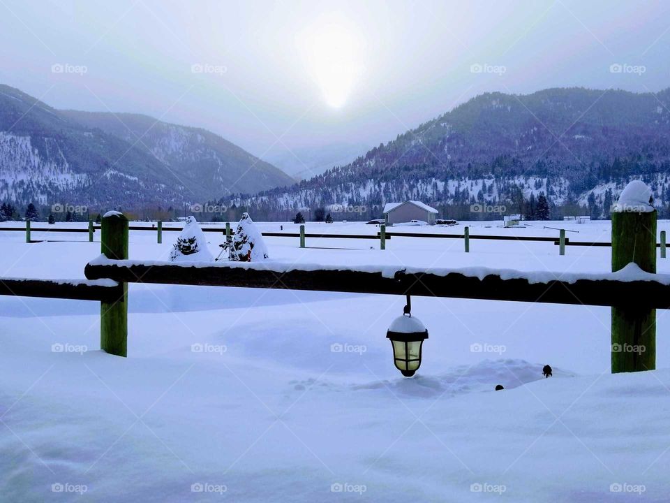sun setting on a snowy fence with a solar lantern. snow covered fences, lanterns, night lights, mountain sunset