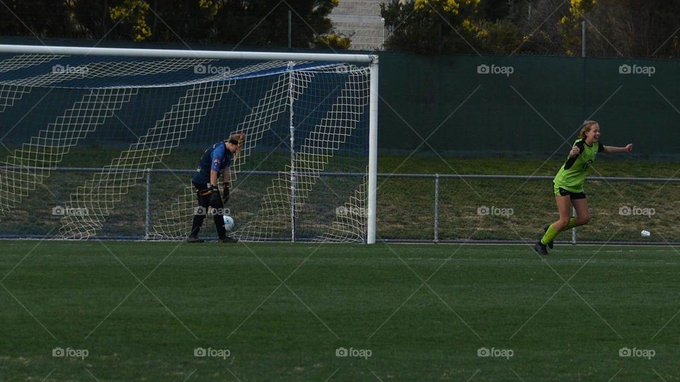 Girl celebrating after scoring the grand final winning goal while the goalkeeper hangs her head.