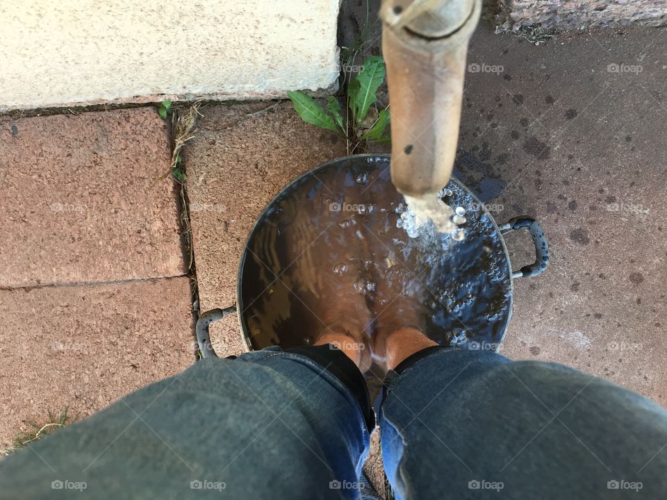 Water pouring into metal bucket from outside tap faucet over bare feet