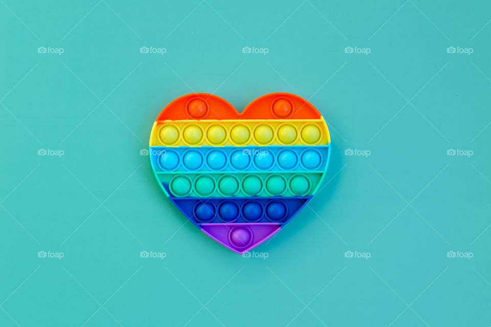 Top view of anti stress sensory toy Pop it rainbow heart on blue background. Popular, trend toys in 2021.