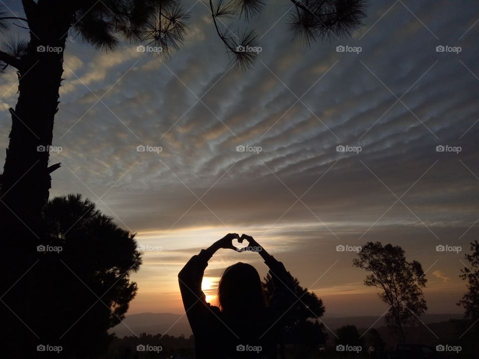 Heart shape with woman's hand in evening sunrise.