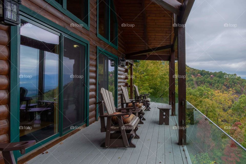 the porch side of a cabin with a line of comfortable chairs facing the beautiful view of the mountains that is also reflected in the sliding glass doors