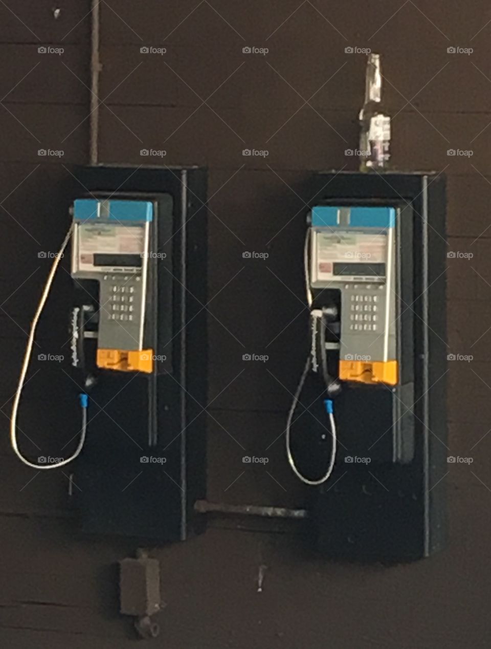 A pair of pay phones with a bottle. 