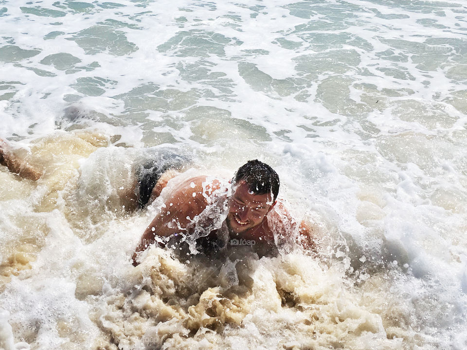 Young man happily smiling being covered by the ocean wave 
