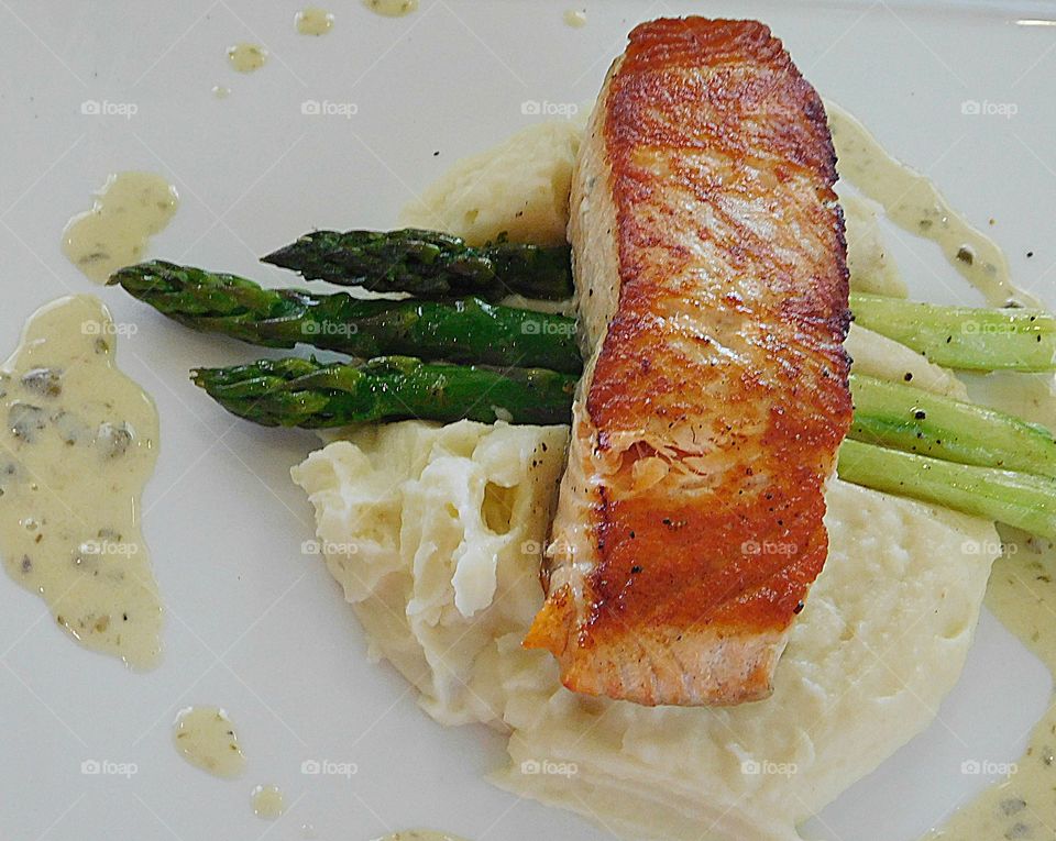 A freshly caught and pan seared Salmon Steak on a bed of mashed potatoes and asparagus outlined with homemade tartar sauce - a meal fit for a king