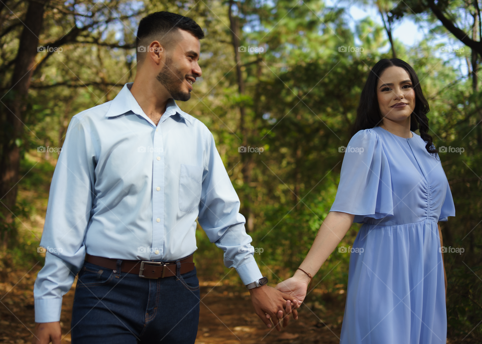 Couples of young people walking in middle of the forest while looking happy into their eyes, in a sunny day.