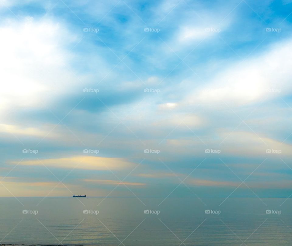 Dreamy ocean view ship in distance on calm glassy ocean at sunrise 