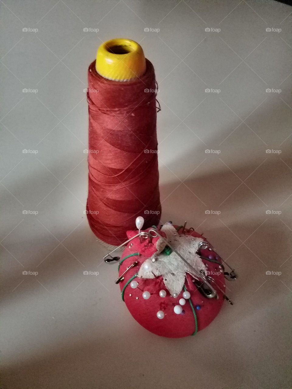 Spool of red thread & red pin cushion full of pins.