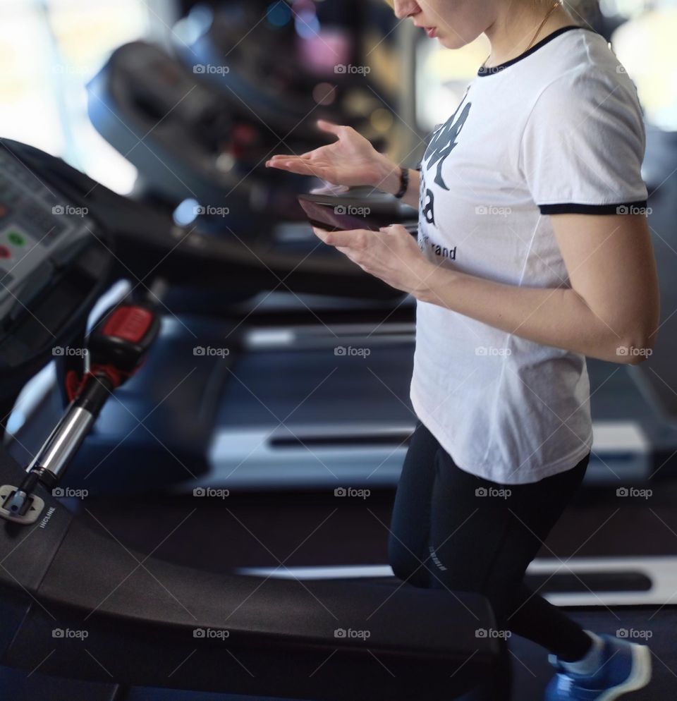 running, treadmill, girl runs, teophone in hands, girl with phone, white t-shirt, gym, sports