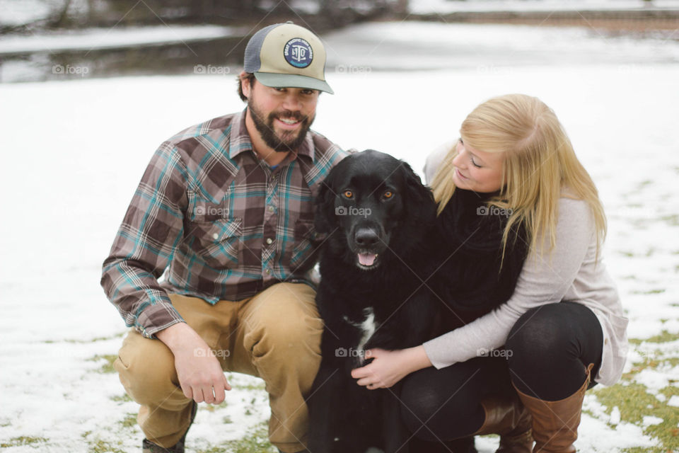 Husband and wife with dog sitting on field during winter
