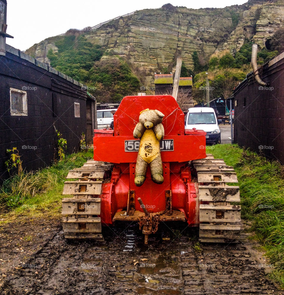 A ragged, mascot teddy bear sits at the helm of this bright red, fishing boat tractor