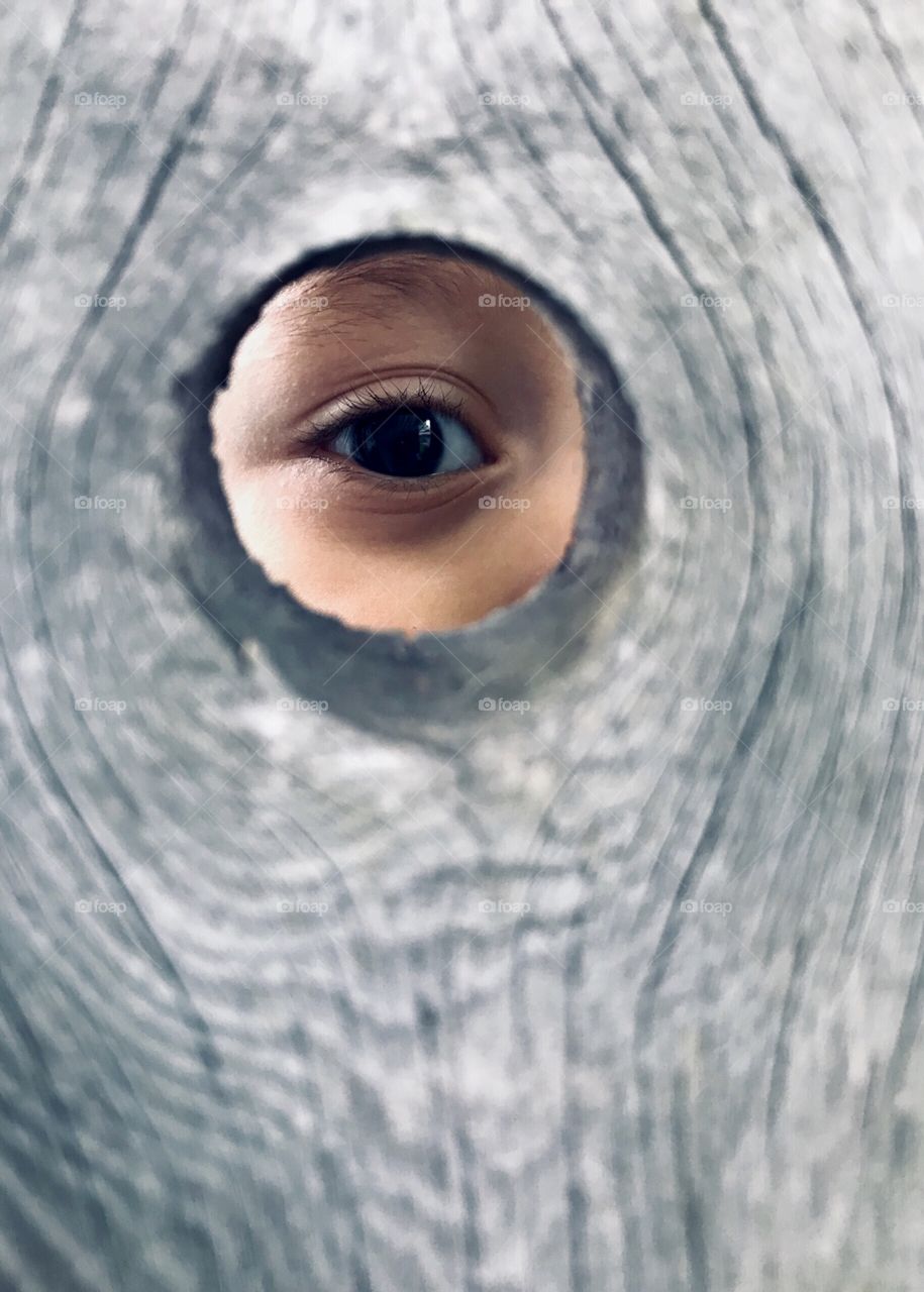 Young child’s eye looking through the hole in a fence