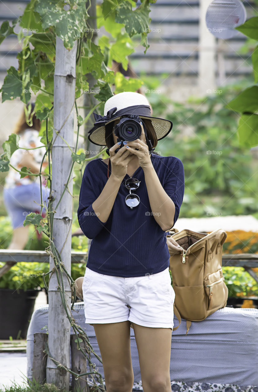 Hand woman holding the camera Taking pictures Background of trees and flowers