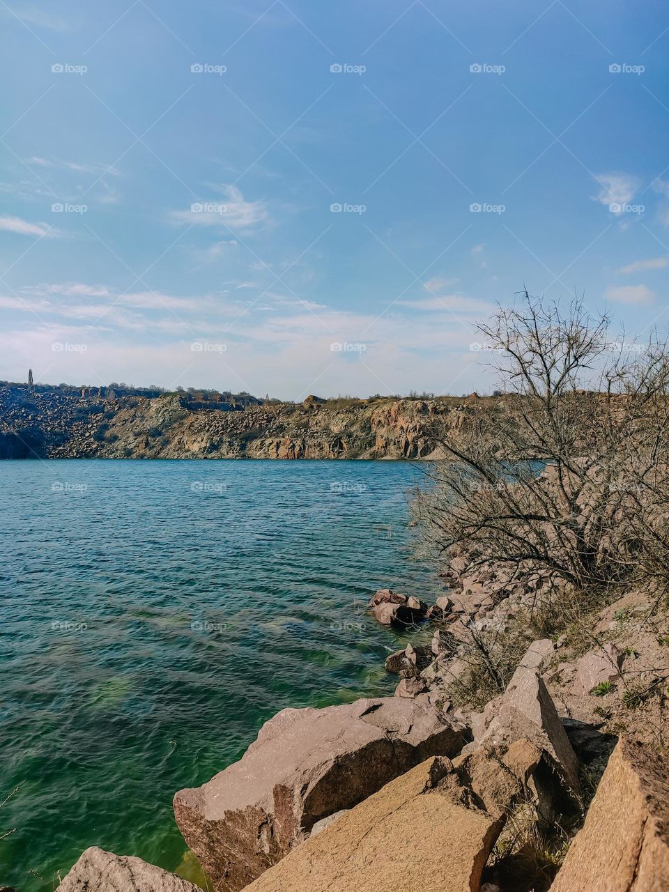 Lake with blue green water in the granite stone career landscape, blue sky, waves on the water, trees without leaves