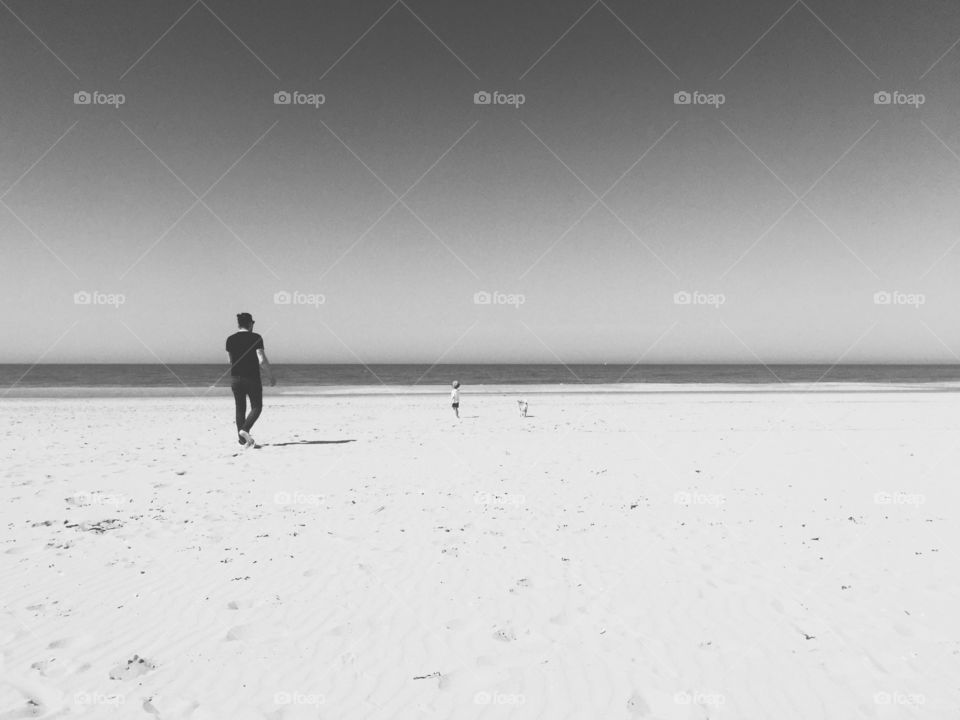 Beachwalk. Father, son and dog on an empty beach in black and white.