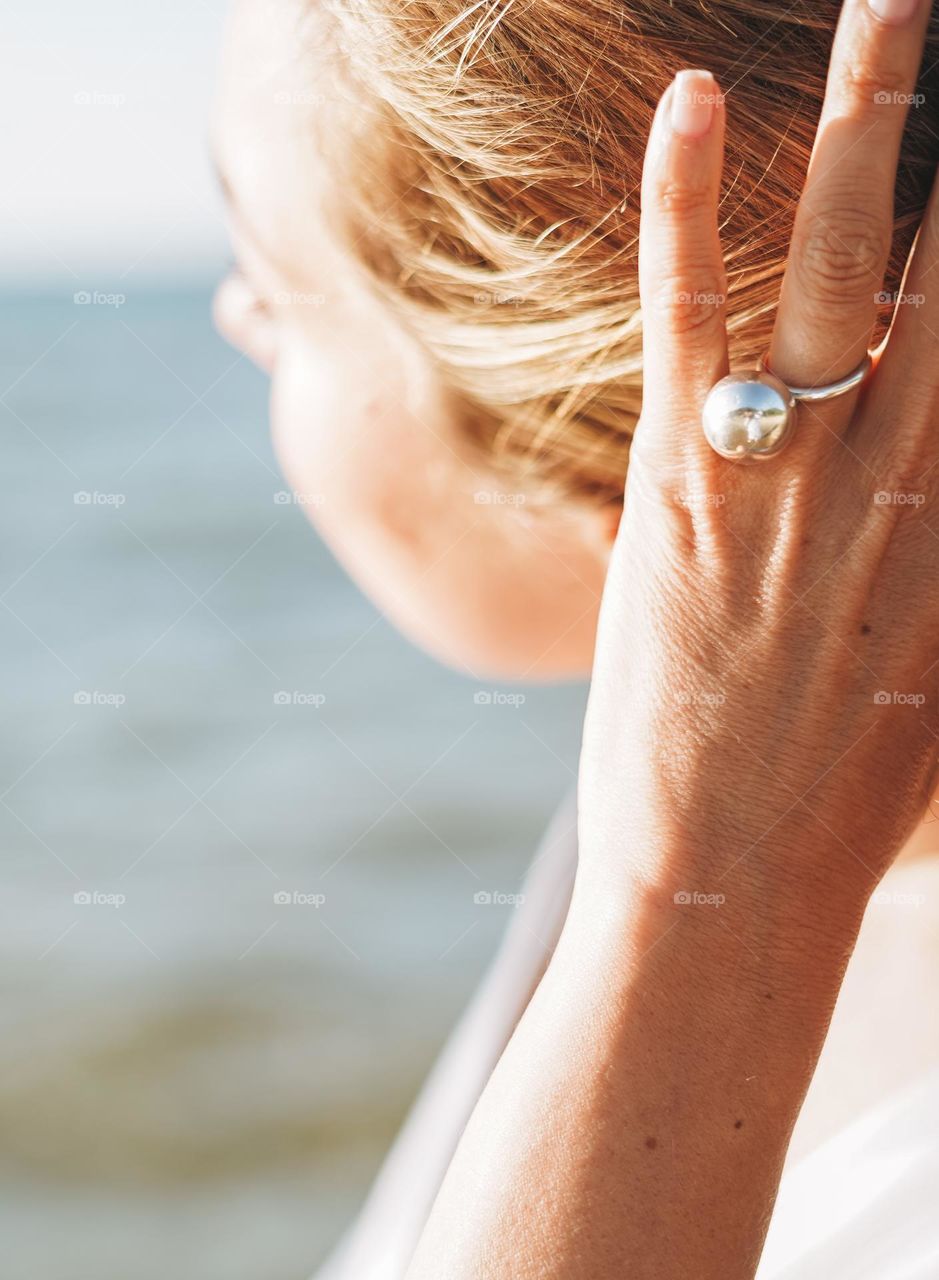 Young woman with beautiful jewellery rings on hands on sea background 