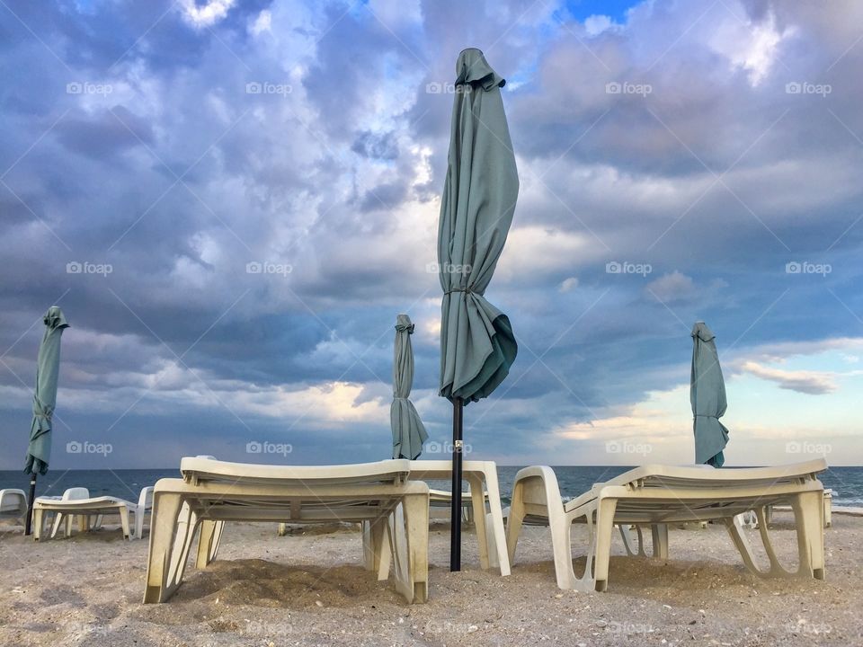 Empty sunbeds on the beach with umbrellas and storm clouds above