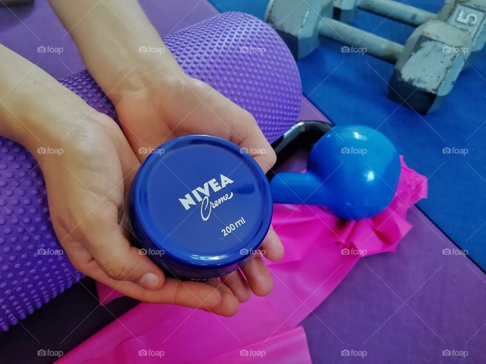 young woman showing a nivea creme product around foam roller and gym equipment