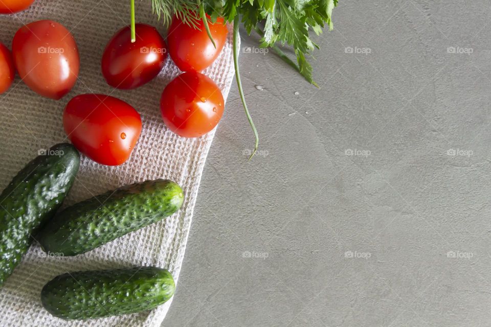 Fresh, bright, juicy vegetables and herbs for preparing salads and other vegetable dishes are on a gray, kitchen worktop.