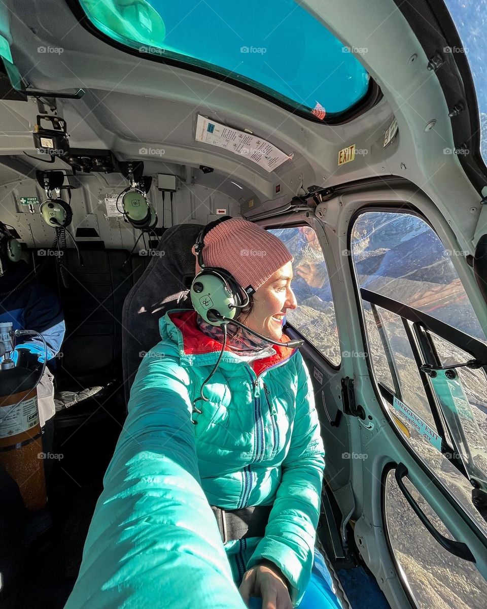 Woman taking a selfie while taking a ride with a helicopter in the mountains.
