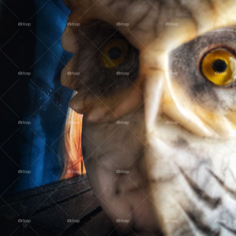 A white marble owl with inset yellow glass eyes glares at the camera from close up. The statue is small and the background is blue.