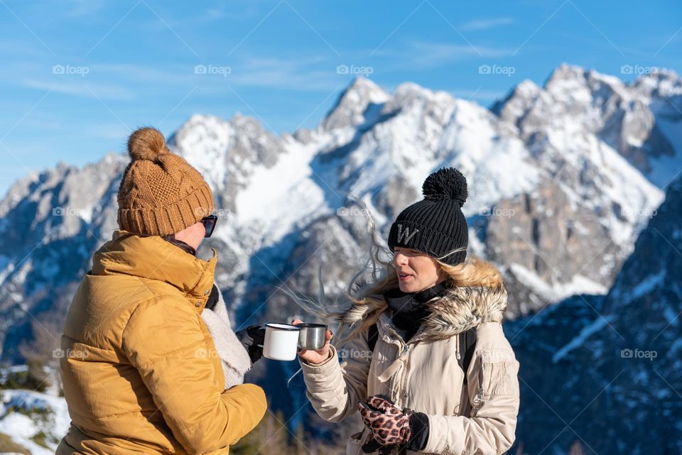 Two friends drinking hot tea on a hike in the mountains in winter