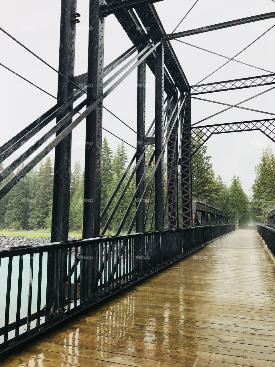 A steel and wood bridge located in Canmore, Alberta, Canada.  It was a rainy day.  Water is flowing under the bridge.