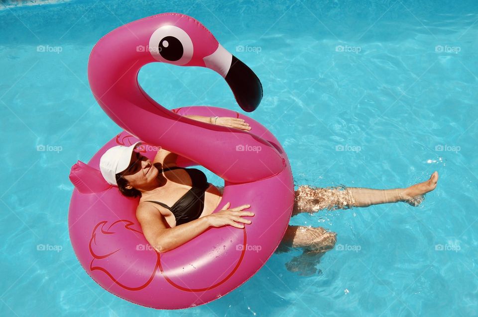 Woman floating with pink flamingo in swimming pool 