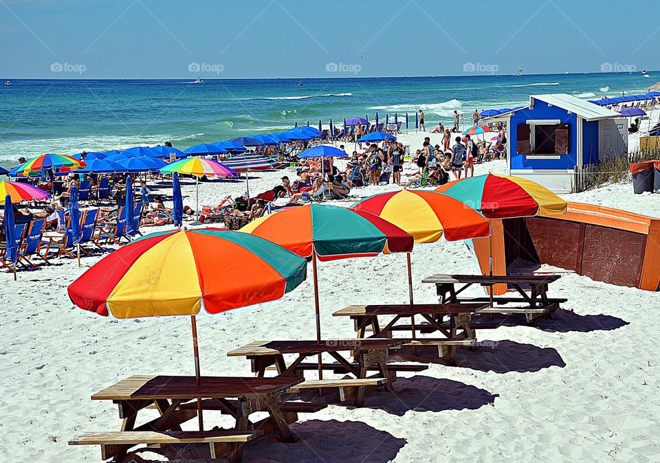 Vibrant beach scene - The background reveals a lively beach with numerous people enjoying the sun and water. The clear, green waters are characteristic of the Emerald Coast