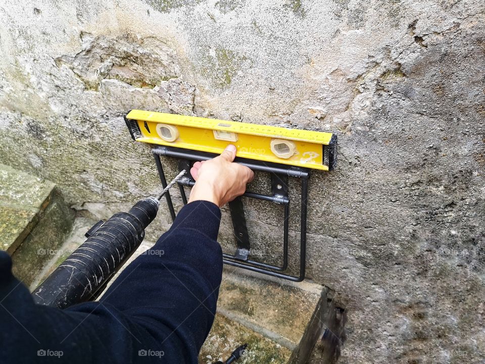 worker makes holes in the wall with a drill to fix a metal support that will serve to contain a garbage pail