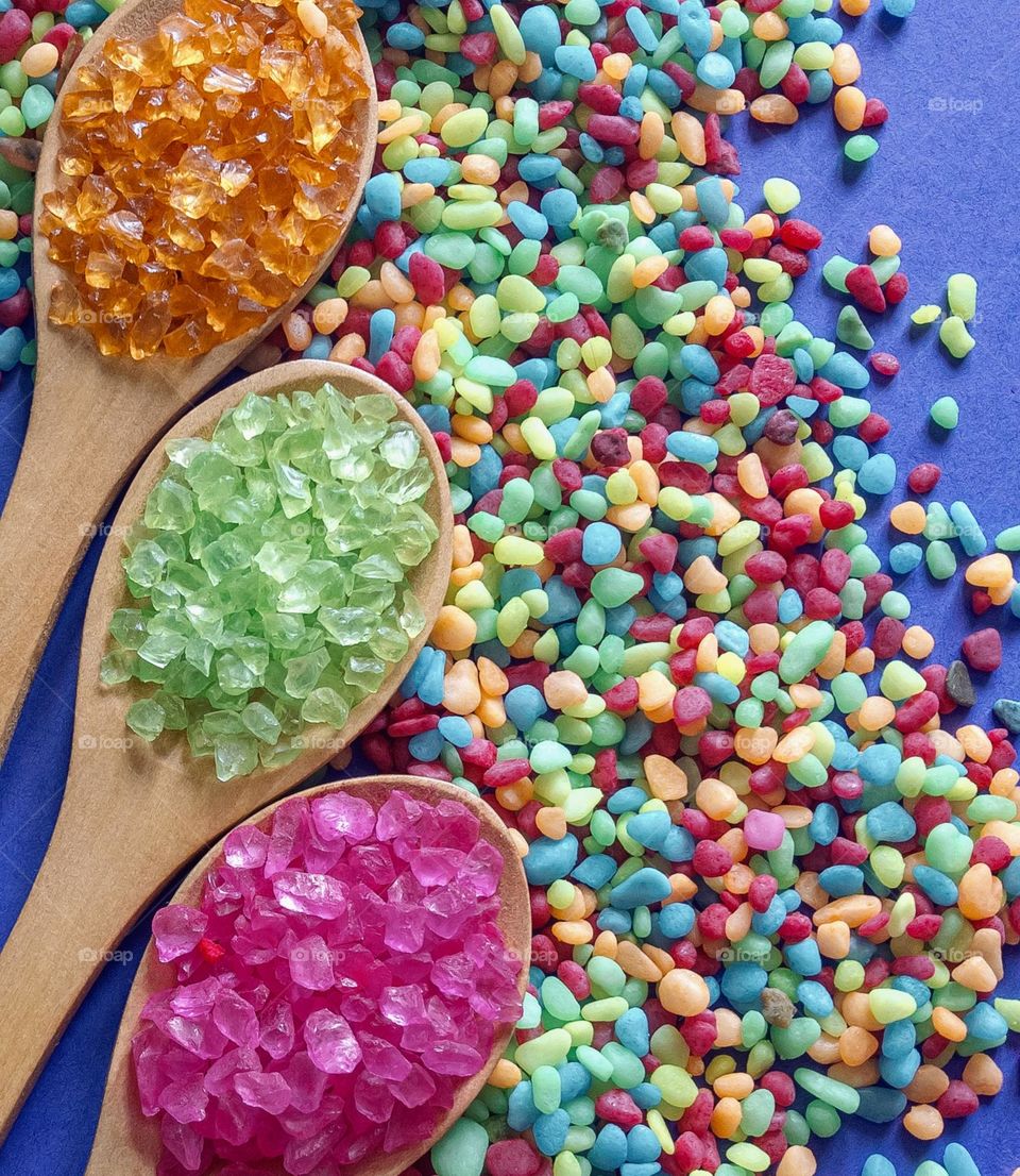 Brightly coloured tiny pebbles and spoonfuls of coloured gravel against blue background 