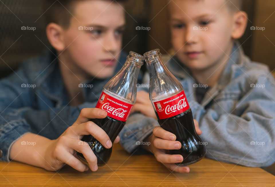 two lovely brothers, dressed in denim clothes, with beautiful hairstyles, are sitting in a cafe and drinking Coca-Cola. communicate, laugh, smile. two guys, two friends