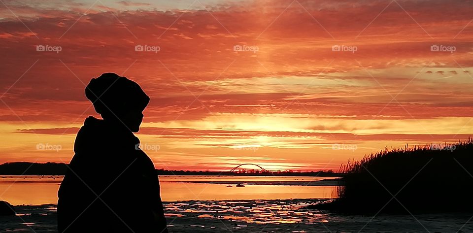 Man sieht einen Sonnenuntergang auf Fehmarn man sieht das Mehr die Fehmarnsundbrücke und ein kleines Kind im Vordergrund.