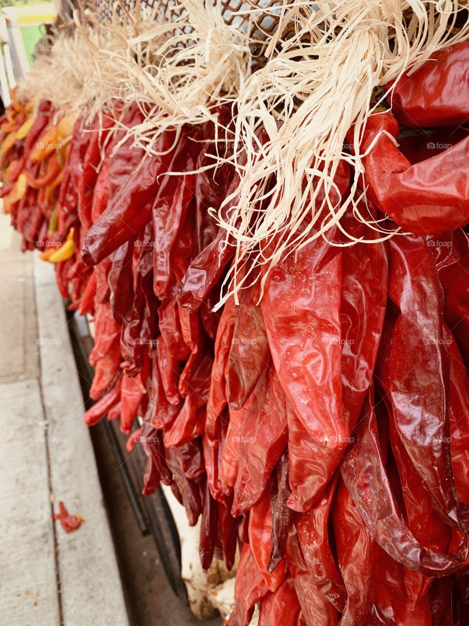 Vivid red, orange, and yellow chilis hang in bunches from a truck at an outdoor farmers market.