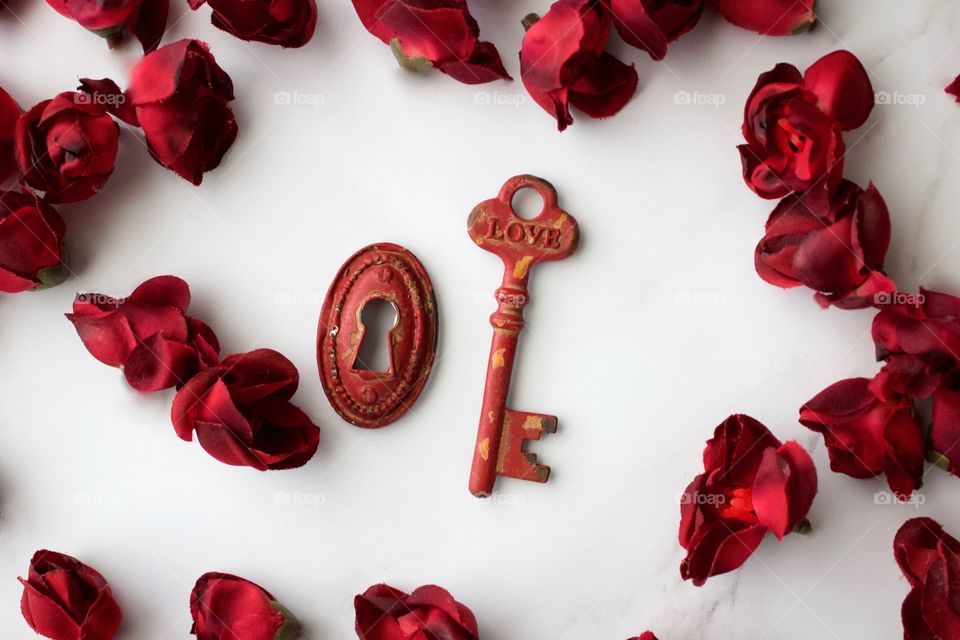 Red, metal, vintage key and keyhole with red, silk rose buds on white marble surface