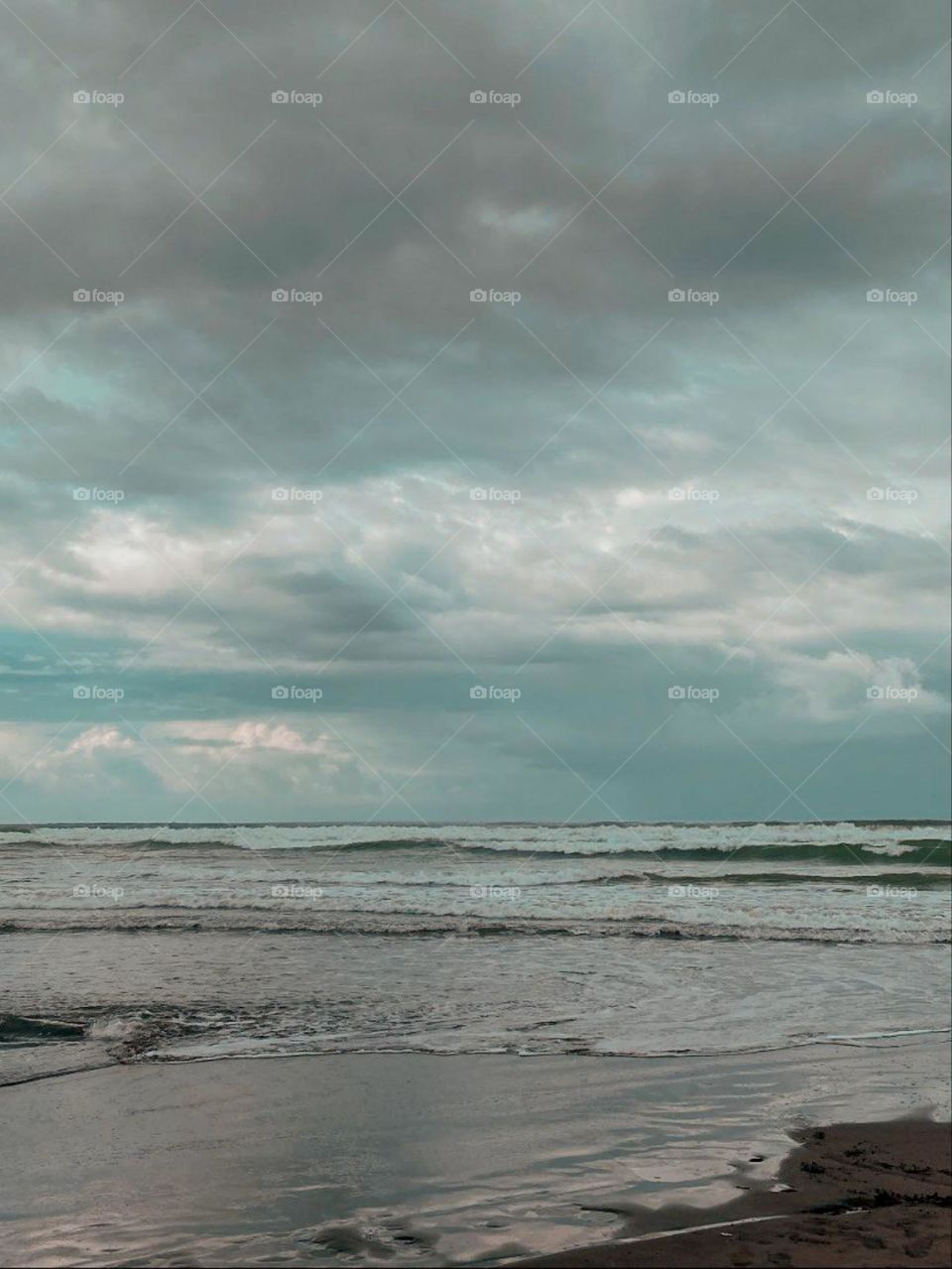 Landscape of a beach view with cloudy skies and calm waves. The color of the sky and sea water depicts a calm and peaceful atmosphere