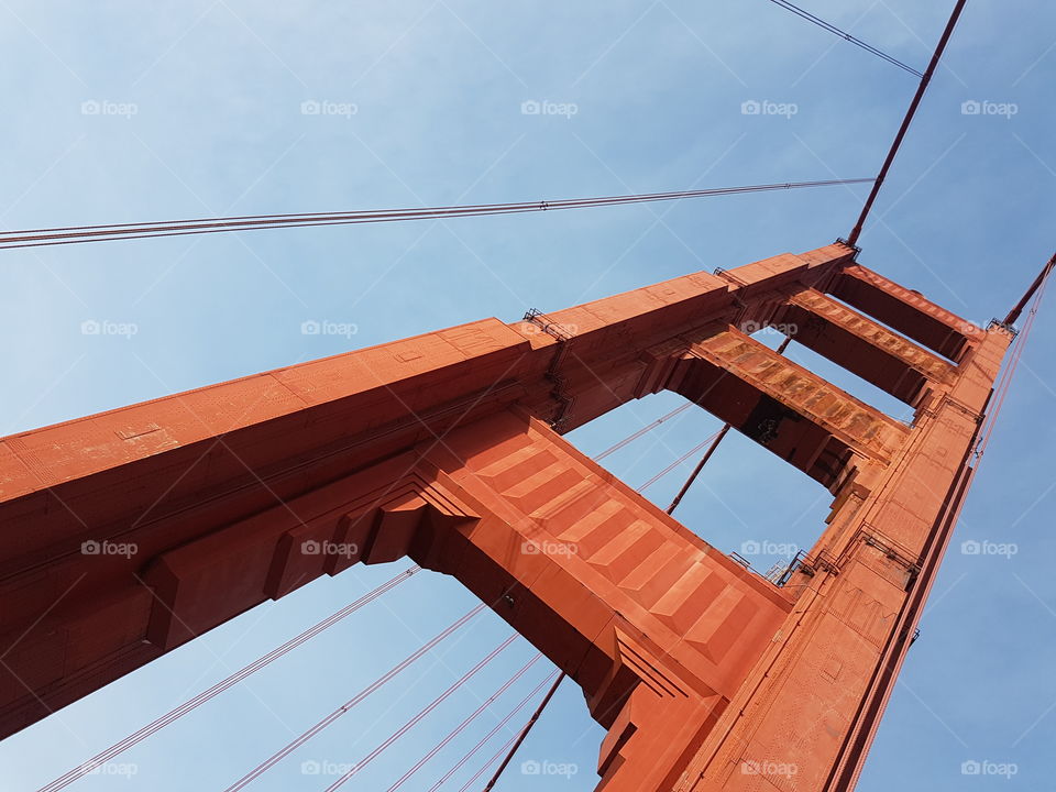 Unique angle view of the famous Red colored Golden Gate Bridge in San Francisco, amazing engineering and architectural design, with cloudy blue sky as a backdrop.