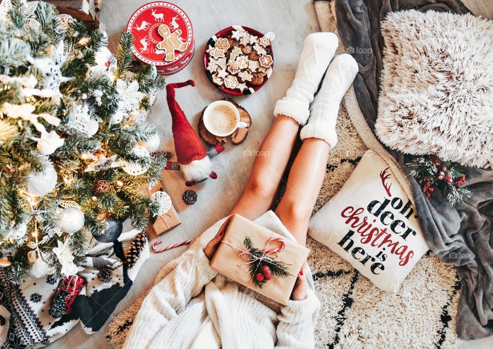 Top view of a woman holding a brown gift box on a carpet beside a Christmas tree