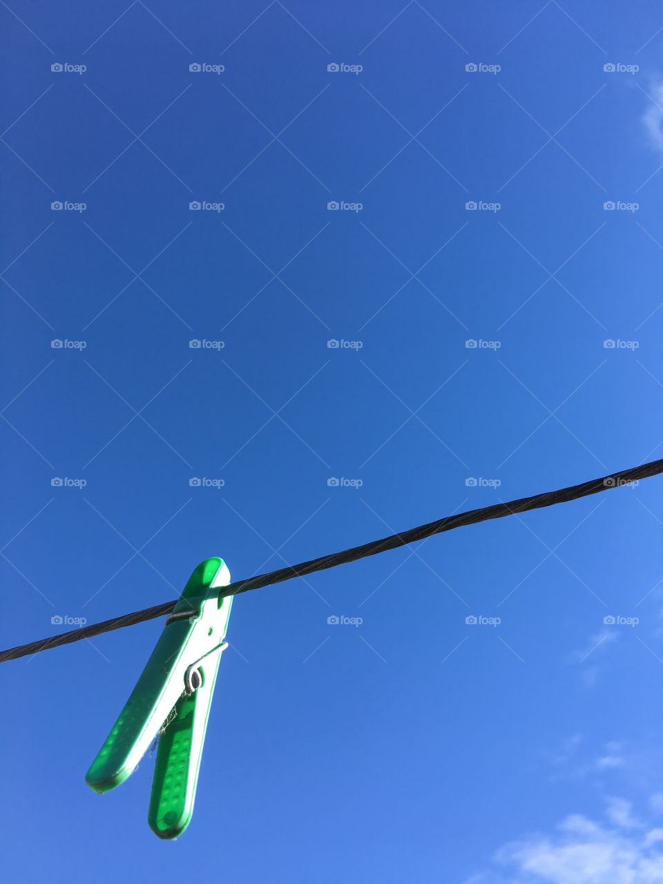 Green plastic clothespin clothes peg hanging on wire outdoor laundry line set against an indigo vivid blue sky in summer minimalistic room for text 