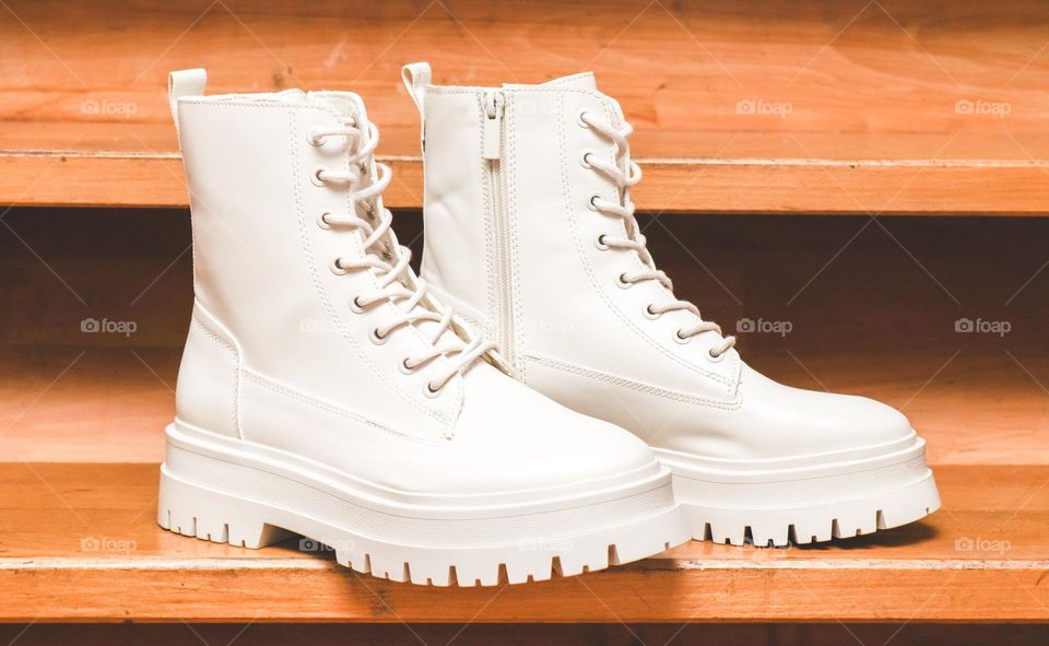 One pair of beautiful white Martens brand boots on a rough tractor sole with lacing stand on the wooden steps of the stairs in the house, side view. The concept of fashionable women's shoes.