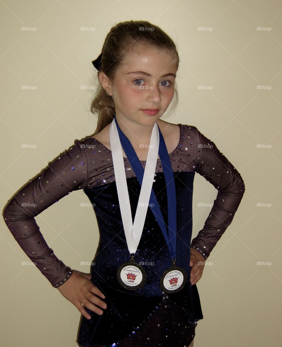 Child poses with first- and third-place medals won from figure skating competition. 