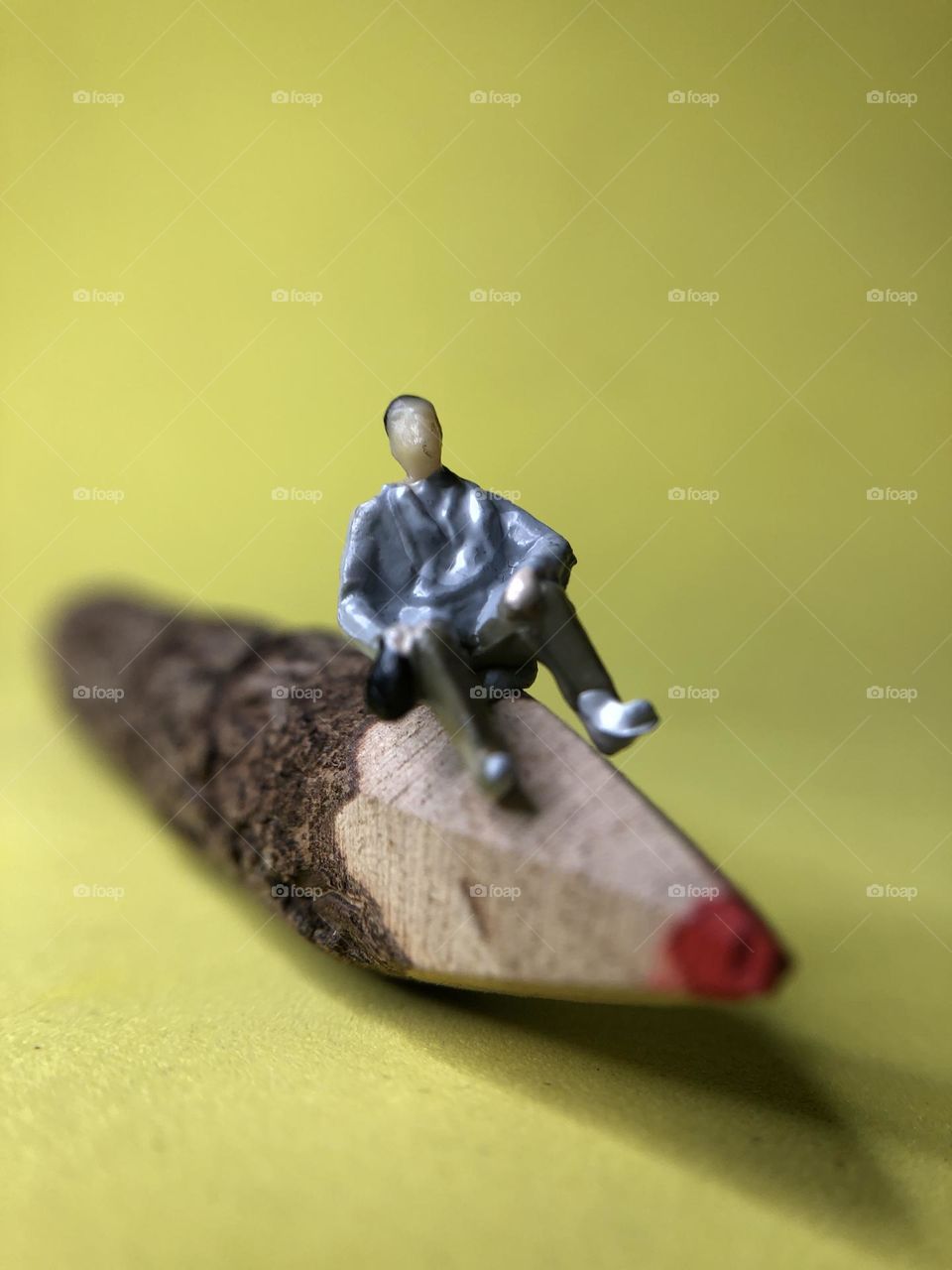 A tiny model person sits on the end of a twig pencil