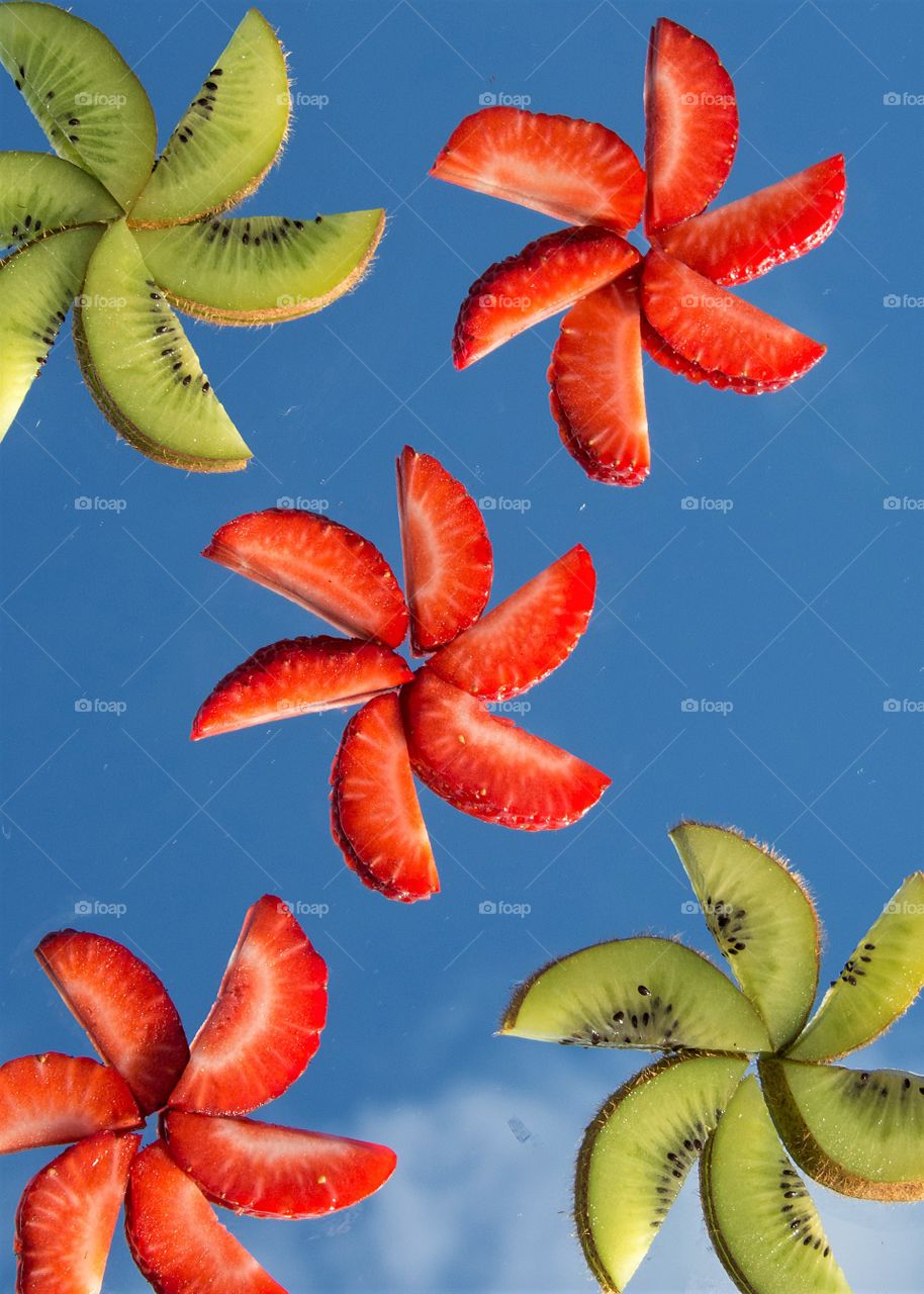 Kiwi and strawberry slices on a mirror reflecting the sky