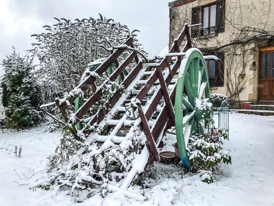 A wooden, wheeled cart outside a French farmhouse in the snow