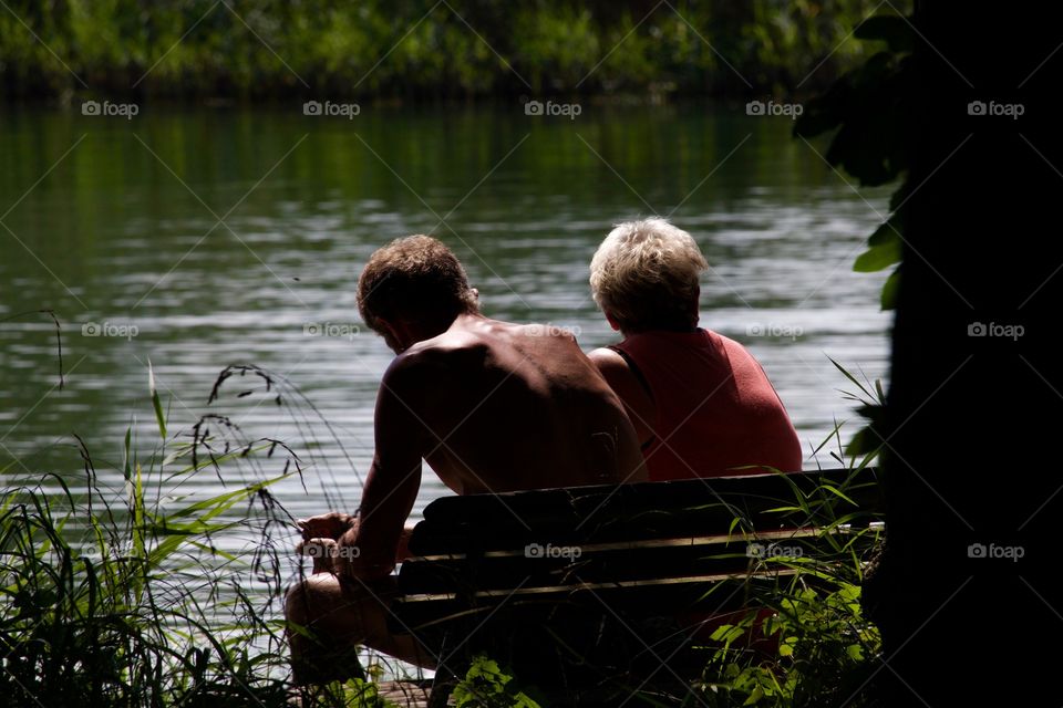 Couple Sitting On Bench By The Lake