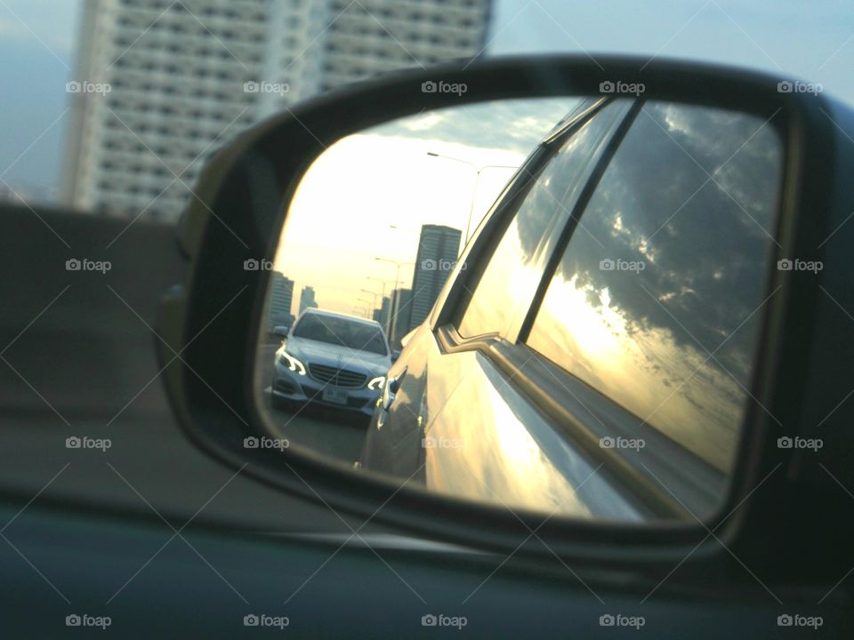 Reflection on the review mirror at sunrise during  on highway, a grey car chasing