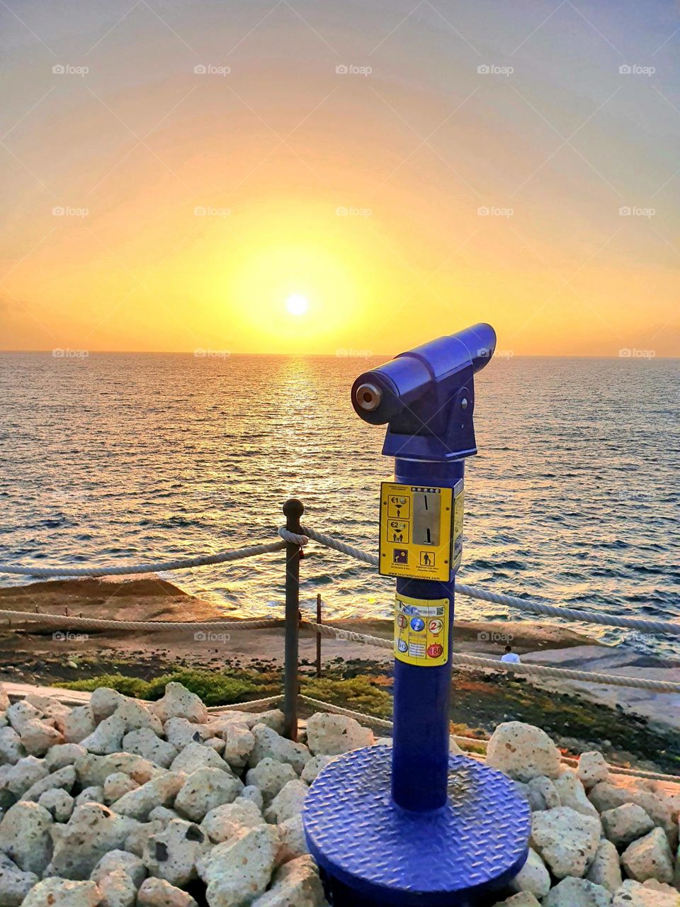 blue telescope by the sea with sunset in the background